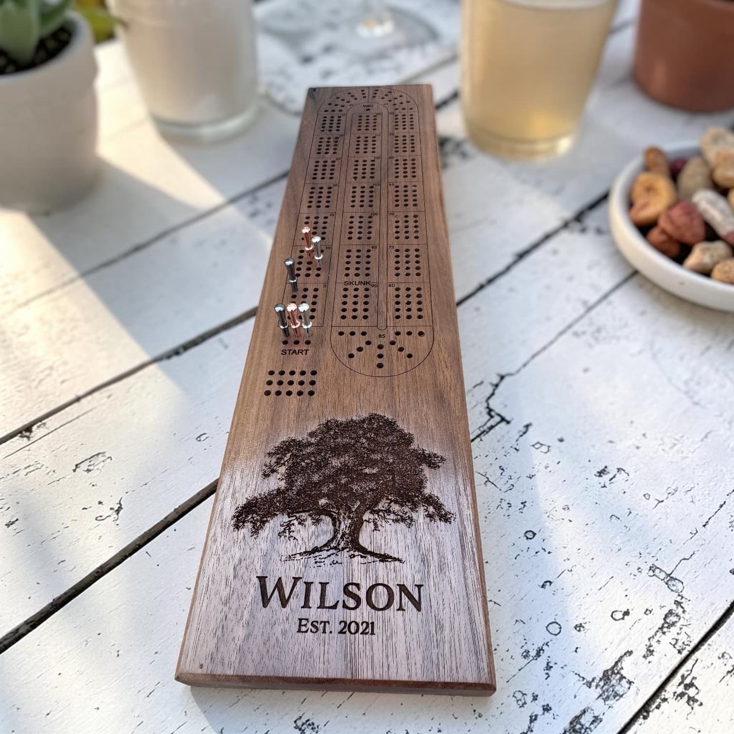 Personalized Black Walnut cribbage board in play on a patio table, engraved with a family name and est. year